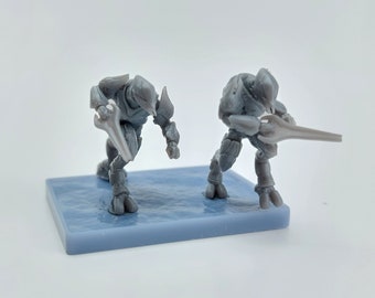 Puede incluir: Dos figuras de acción de plástico gris de guerreros alienígenas sosteniendo armas de energía. Las figuras están de pie sobre una base de plástico gris.