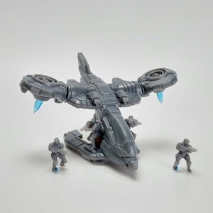 May include: A grey plastic toy helicopter with two rotating blades and four figures inside. The helicopter has a detailed design with a cockpit and a cargo bay. The figures are wearing military uniforms and holding weapons.