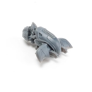May include: A gray plastic model of a futuristic spaceship with a detailed design. The spaceship has a rounded body and two wings.