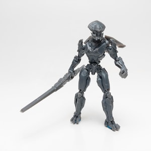 May include: A gray plastic action figure of a robot holding a sword. The robot has a detailed design and is posed in a fighting stance.