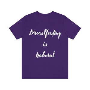 Puede incluir: Una camiseta morada con el texto blanco "Breastfeeding is Natural" en un estilo manuscrito. La camiseta tiene mangas cortas y cuello redondo, adecuada para ropa casual.