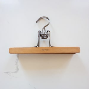 May include: A wooden clothes hanger with a metal clip and hook. The hanger is labeled "Tevco".