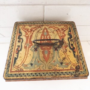 K&ouml;nnte beinhalten: Vintage Metallbox mit einem dekorativen Blumendesign in Gelb-, Orange-, Gr&uuml;n- und Blaut&ouml;nen. Die Box hat einen Metallgriff und einen Holzboden.