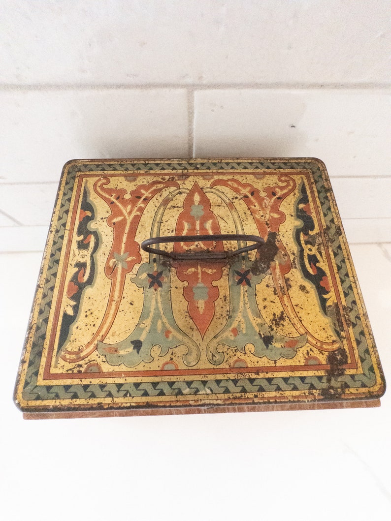 K&ouml;nnte beinhalten: Vintage Metallbox mit einem dekorativen Blumendesign in Gelb-, Orange-, Gr&uuml;n- und Blaut&ouml;nen. Die Box hat einen Metallgriff und einen Holzboden.