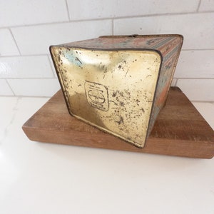 K&ouml;nnte beinhalten: Vintage-Metalldose mit goldenem Boden und buntem Design. Die Dose hat einen abgenutzten, alten Look und ein Logo mit den Buchstaben "E & J" in einem Kreis.