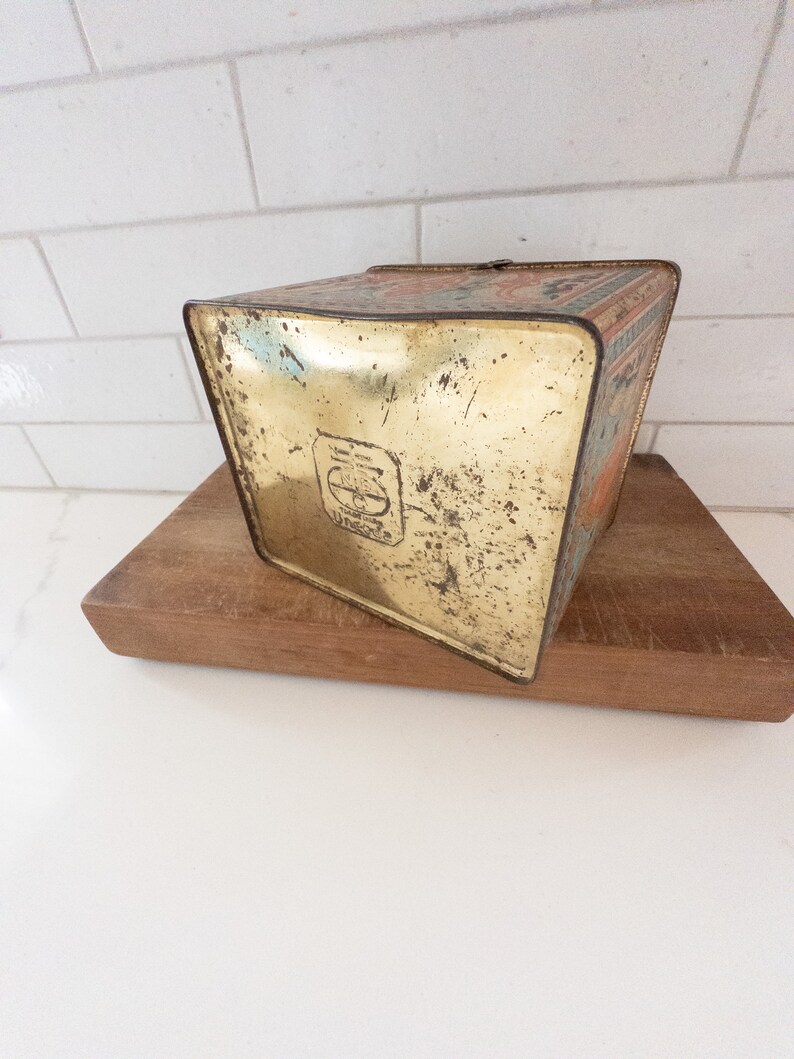 K&ouml;nnte beinhalten: Vintage-Metalldose mit goldenem Boden und buntem Design. Die Dose hat einen abgenutzten, alten Look und ein Logo mit den Buchstaben "E & J" in einem Kreis.