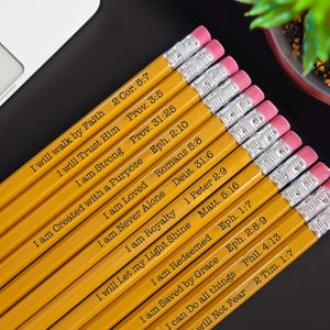 May include: A set of yellow pencils with inspirational bible verses printed on them. The verses include "I will walk by Faith", "I will Trust Him", "I am Strong", "I am Created with a Purpose", "I am Loved", "I am Never Alone", "I am Royalty", "I will Let my Light Shine", "I am Redeemed", "I am Saved by Grace", "I can Do all things", "I will Not Fear".