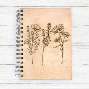 May include: A wooden spiral bound journal with a wood-burned design of various flowers and leaves.