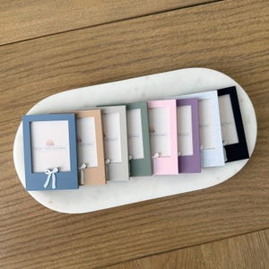 May include: A collection of small, rectangular picture frames in various pastel colors, including blue, tan, green, pink, and purple. Each frame has a bow detail at the bottom and the text "PRINT PURPOSEFULLY" or "WONDERFULLY" printed on the inside.