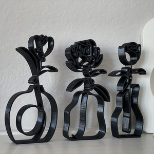May include: Three black metal sculptures of stylized flowers in vases. The sculptures are abstract and minimalist in design.
