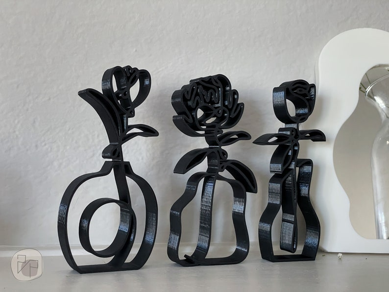 May include: Three black metal sculptures of stylized flowers in vases. The sculptures are abstract and minimalist in design.