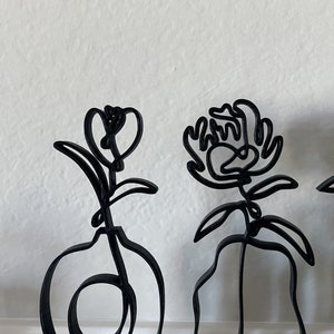 May include: Three black metal sculptures of flowers. The sculptures are abstract and minimalist in design. The flowers are all different shapes and sizes.