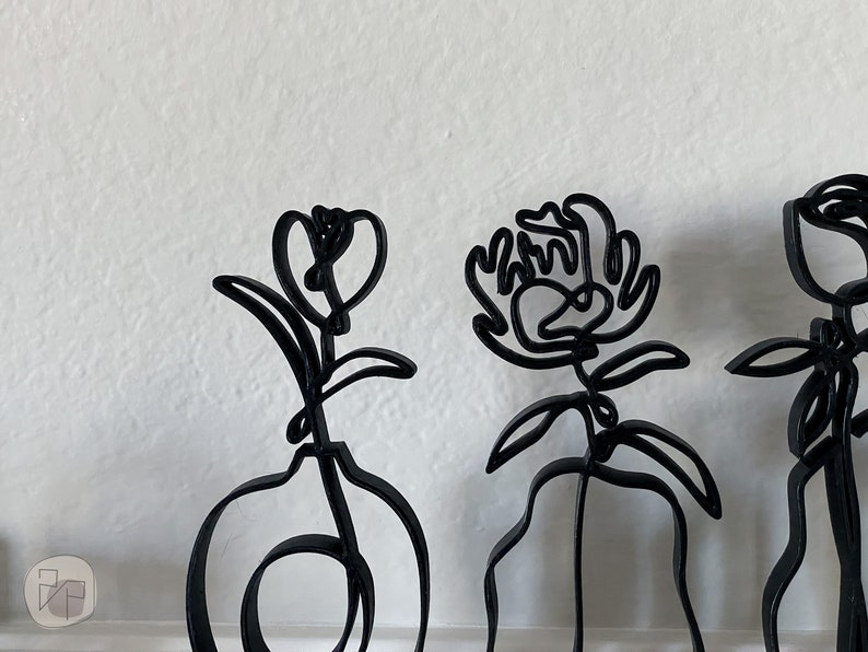 May include: Three black metal sculptures of flowers. The sculptures are abstract and minimalist in design. The flowers are all different shapes and sizes.