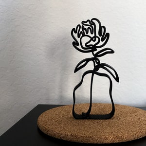 May include: Black metal sculpture of a flower in a vase. The flower is stylized and has a single stem with leaves. The vase is a simple, abstract shape.