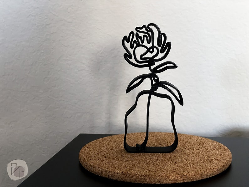 May include: Black metal sculpture of a flower in a vase. The flower is stylized and has a single stem with leaves. The vase is a simple, abstract shape.