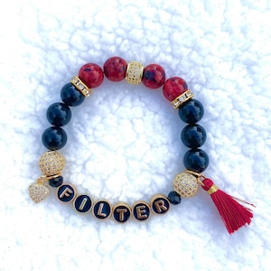 May include: A black and red beaded bracelet with gold accents and a red tassel. The bracelet features the word "FILTER" spelled out in gold letters on black beads.