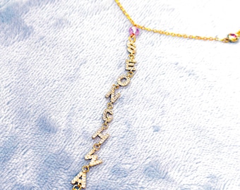 May include: A gold chain necklace with a pink gem charm and a star charm. The chain has the word "HAPPY" spelled out in gold letters with small diamonds.