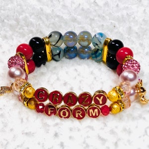May include: A multi-strand bracelet with pink, red, black, and gold beads. The bracelet has a charm with the words "CRAZY FOR" on it.