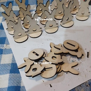 Può includere: Un set di forme di coniglio in legno grezzo, alcune assemblate in porta biglietti da visita a forma di coniglio. Le forme di coniglio sono pronte per essere dipinte o tinte. Il testo "by ViveDo3D" è visibile nell'immagine.