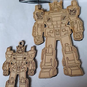 May include: Two wooden robot ornaments, one larger than the other. Both are detailed with lines and shapes, resembling a robot.