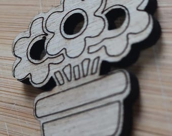 Puede incluir: Un recorte de madera de una maceta con tres flores. Las flores son simples y tienen un círculo en el centro. La maceta es un simple rectángulo con la parte superior redondeada.