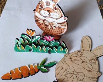 May include: Two wooden bunny figurines, one painted brown with white accents and the other unpainted, with a carrot and green grass.