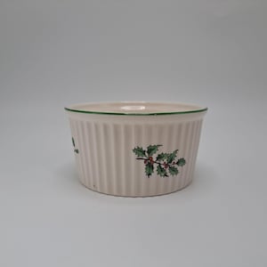 Puede incluir: Un ramequín de cerámica color crema con laterales acanalados verticales y un borde verde. El ramequín está decorado con un diseño de acebo y bayas en verde y rojo. Una pieza festiva para servir porciones individuales.