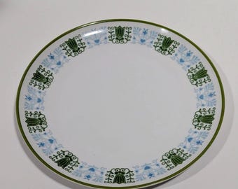 May include: A round white dinner plate featuring a decorative border pattern of alternating dark green tulip motifs and light blue floral scrollwork. The rim of the plate is finished with a thin dark green band, creating a clean and symmetrical design.