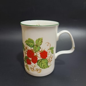 Peut inclure: Mug en céramique blanche avec un bord et une anse verts. Le mug est orné d'un motif de framboises rouges, de feuilles vertes et de fleurs blanches. Un design classique pour les boissons chaudes.