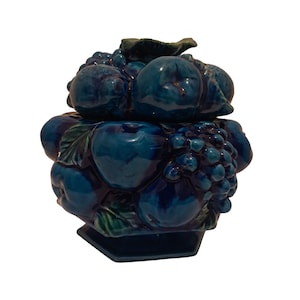 May include: A teal ceramic fruit basket with a lid. The basket is adorned with sculpted fruits, including apples and grapes, and green leaves. The base is hexagonal. The glossy finish enhances the details of the fruit.