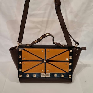 Bolso tipo cartera de piel sintética de color marrón y naranja con detalles de tachuelas doradas