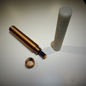 K&ouml;nnte beinhalten: Ein goldfarbenes Metallrohr mit einer schwarzen Batterie im Inneren. Das Rohr ist offen und der Deckel ist abgenommen. Der Deckel ist ebenfalls aus goldenem Metall. Neben dem goldenen Rohr befindet sich ein wei&szlig;es Plastikrohr.