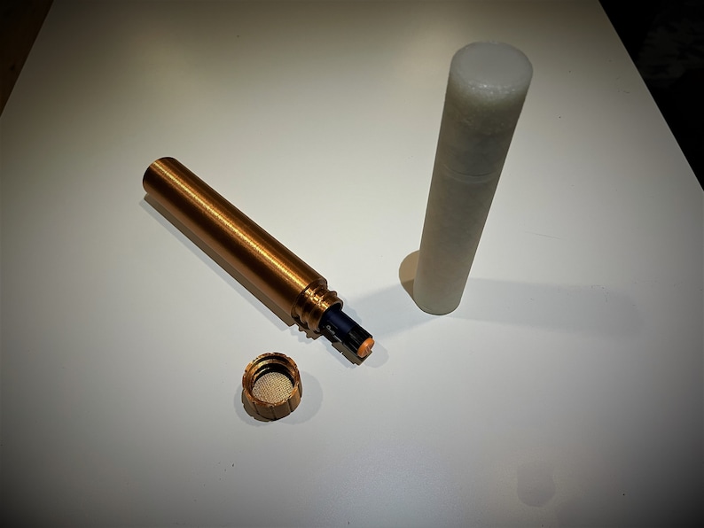 K&ouml;nnte beinhalten: Ein goldfarbenes Metallrohr mit einer schwarzen Batterie im Inneren. Das Rohr ist offen und der Deckel ist abgenommen. Der Deckel ist ebenfalls aus goldenem Metall. Neben dem goldenen Rohr befindet sich ein wei&szlig;es Plastikrohr.
