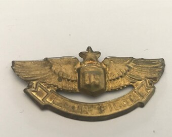 Puede incluir: Un pin de metal dorado con una estrella, alas y el texto "US ARMY PILOT".