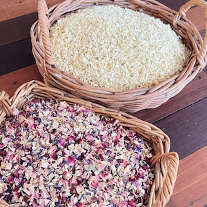 Op de afbeelding: Twee rieten manden gevuld met gedroogde bloemblaadjes. Eén mand bevat crèmekleurige bloemblaadjes, de andere een mix van roze, paarse en blauwe bloemblaadjes. Geplaatst op een houten oppervlak.