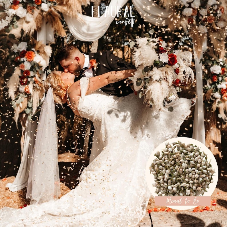 K&ouml;nnte beinhalten: Eine Hochzeitsszene mit einem Brautpaar, das sich unter einem Blumenbogen k&uuml;sst. Die Braut tr&auml;gt ein wei&szlig;es Kleid und einen Schleier und h&auml;lt einen Blumenstrau&szlig;. Konfetti f&auml;llt um sie herum. Der Text "FLORAE confetti" und "Meant to Be" ist enthalten.