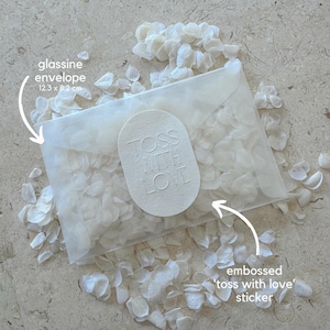 May include: A glassine envelope, 12.3 x 8.2 cm, filled with white petals. An embossed sticker on the envelope reads "TOSS WITH LOVE". White petals are scattered around the envelope, creating a delicate, romantic aesthetic.
