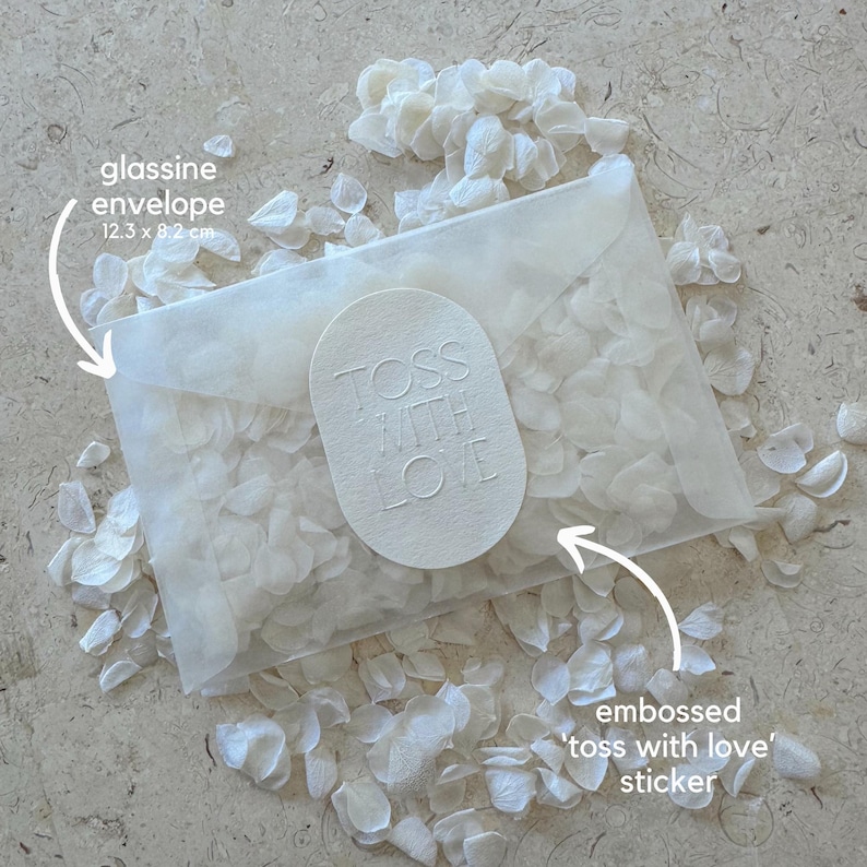 May include: A glassine envelope, 12.3 x 8.2 cm, filled with white petals. An embossed sticker on the envelope reads "TOSS WITH LOVE". White petals are scattered around the envelope, creating a delicate, romantic aesthetic.