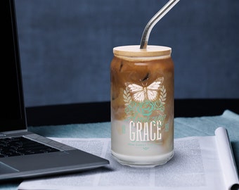 Puede incluir: Una lata de vidrio para café helado con tapa de madera y una pajita de metal. La lata tiene un diseño de mariposa y flores con el texto "Amazing Grace How Sweet The Sound".