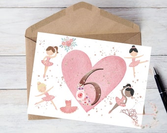 May include: A birthday card featuring a pink heart with the number 6, surrounded by illustrations of ballerinas in pink tutus. The card is inside a brown envelope, with a black pen visible.