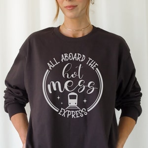 May include: A dark gray sweatshirt with a white graphic design that says "All aboard the hot mess express" with a train icon in the middle of the text.