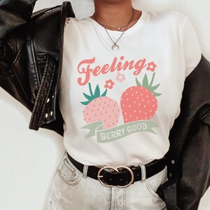 May include: White t-shirt with a graphic of two strawberries and the text "Feeling Berry Good".