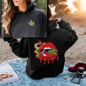 May include: Black hoodie with a green cannabis leaf on the front and a red dripping mouth with a cannabis leaf and a joint on the back.