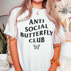 May include: White t-shirt with black text that reads "Anti Social Butterfly Club" and a black butterfly graphic.