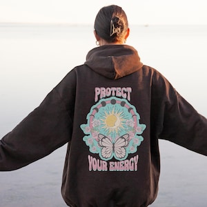 May include: A brown hoodie with a graphic print on the back. The graphic features a sun, moon, and butterfly with the text "Protect Your Energy".