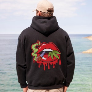 May include: Black hooded sweatshirt with a graphic print of a red mouth with a green cannabis leaf and a lit joint. The mouth is dripping red.