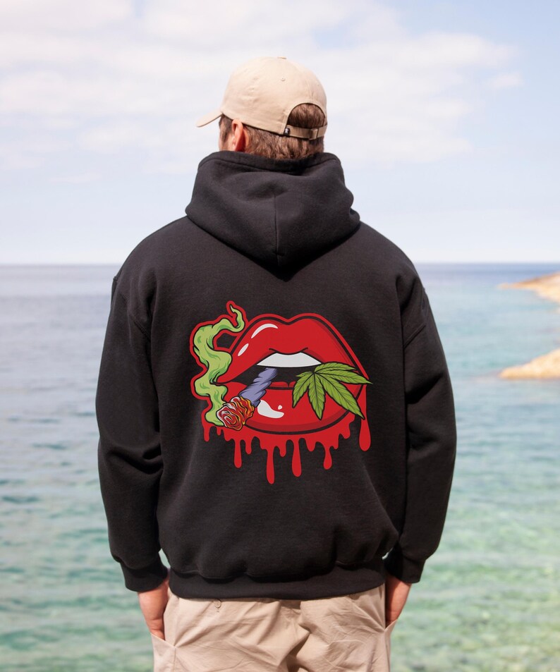 May include: Black hooded sweatshirt with a graphic print of a red mouth with a green cannabis leaf and a lit joint. The mouth is dripping red.
