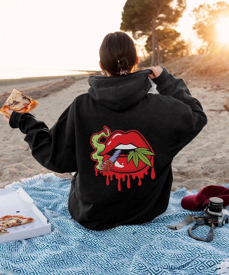 May include: Black hooded sweatshirt featuring a graphic of a red mouth with a marijuana leaf and a joint sticking out. The mouth is dripping red.