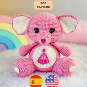 Pode incluir: Um brinquedo de elefante rosa feito à mão em crochê, com detalhes brancos nas orelhas e na barriga. O elefante tem olhos de segurança pretos e um nariz em forma de coração. A barriga apresenta um círculo branco com um desenho rosa. A imagem inclui o texto "PDF PATTERN".