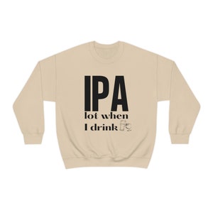 Könnte beinhalten: Beiges Sweatshirt mit Rundhalsausschnitt und dem Text "IPA lot when I drink" in schwarzen Blockbuchstaben. Darunter befinden sich zwei kleine schwarze Illustrationen eines Bierglases und eines Pintglases. Das Sweatshirt hat lange Ärmel und einen runden Ausschnitt.